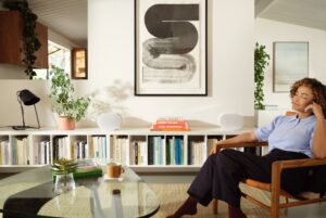 A woman sitting on a wooden chair listening to two white Sonos Era 300